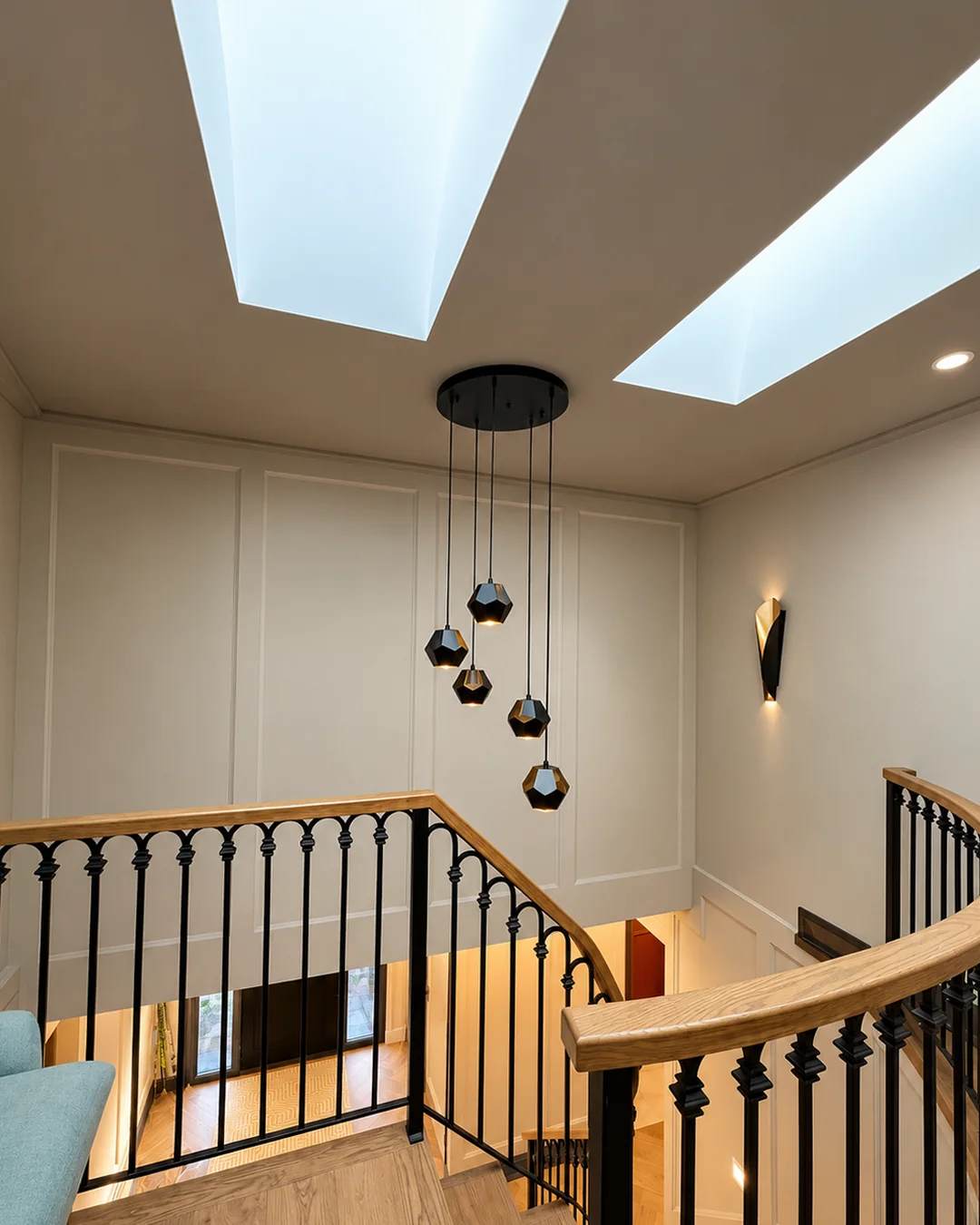 Curved staircase with a stained oak handrail under skylights and geometric pendant lights