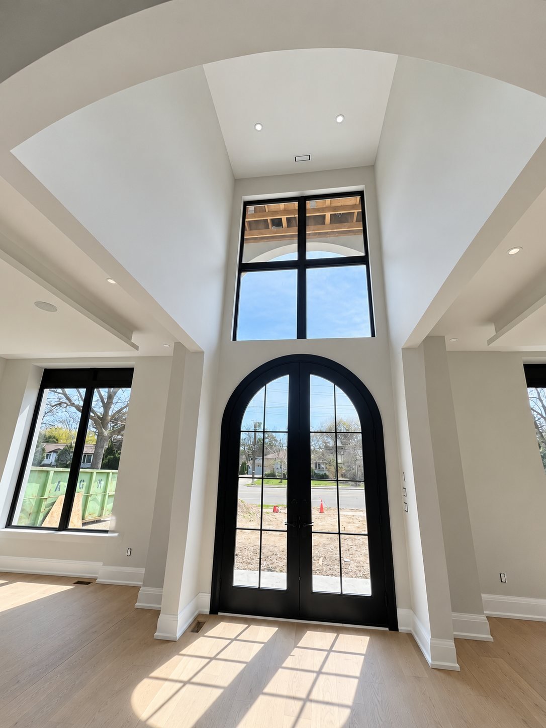 Double-height entry with freshly painted walls and an arched black door, during construction