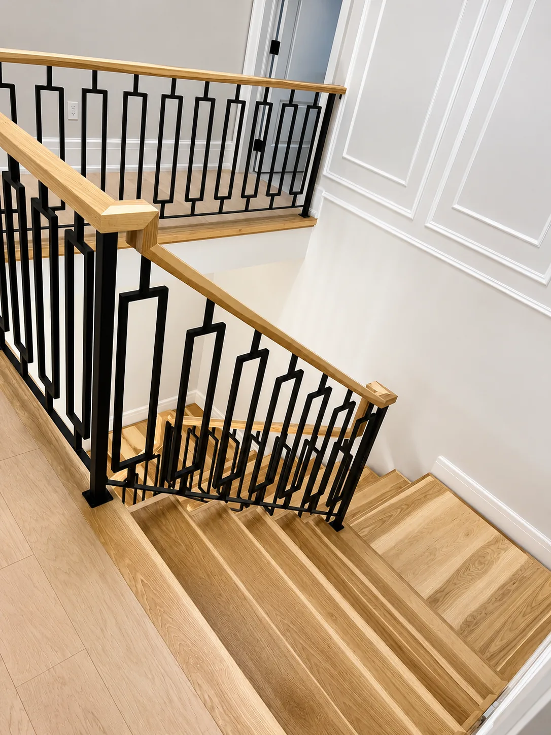 Stair landing with a stained oak handrail and black geometric balusters