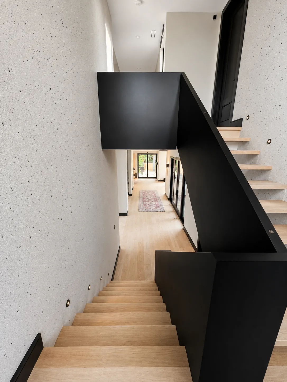 Oak staircase with a black painted stringer leading down to a hallway