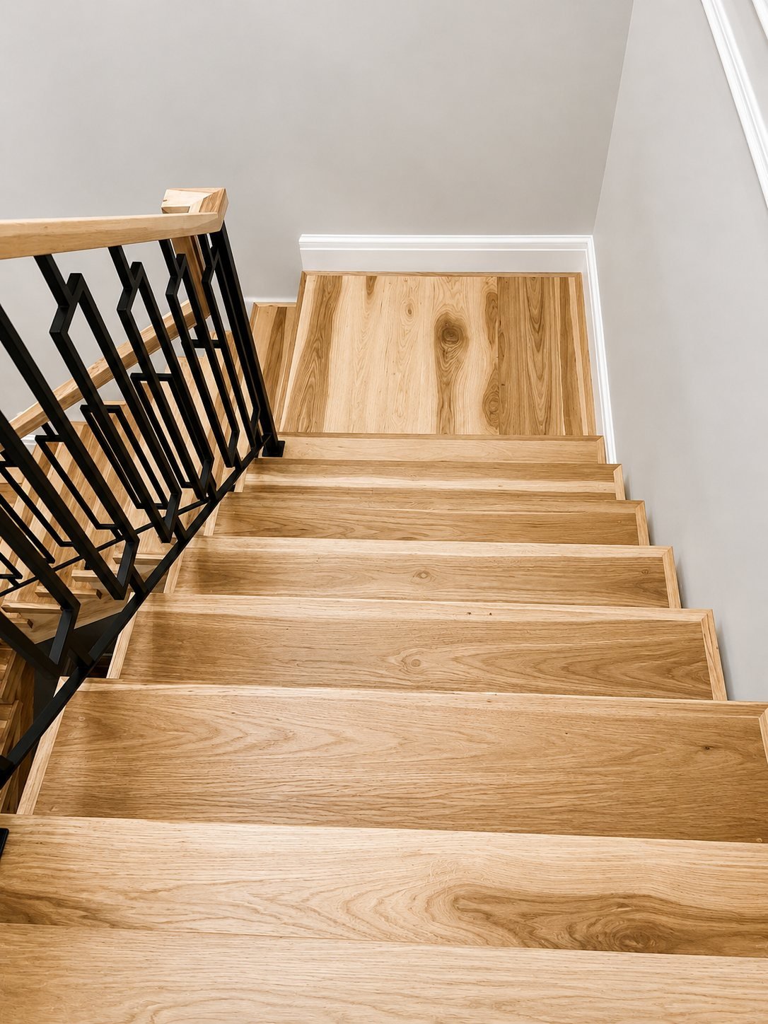 Oak stair treads with a stained handrail and black geometric balusters, seen from above