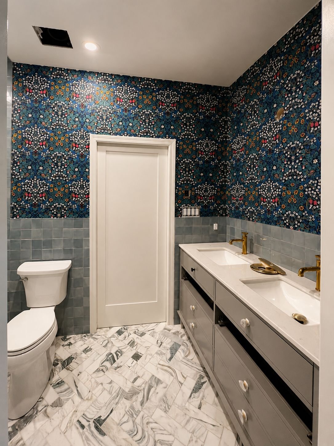 Bathroom with colourful botanical wallpaper above blue tile and a double vanity