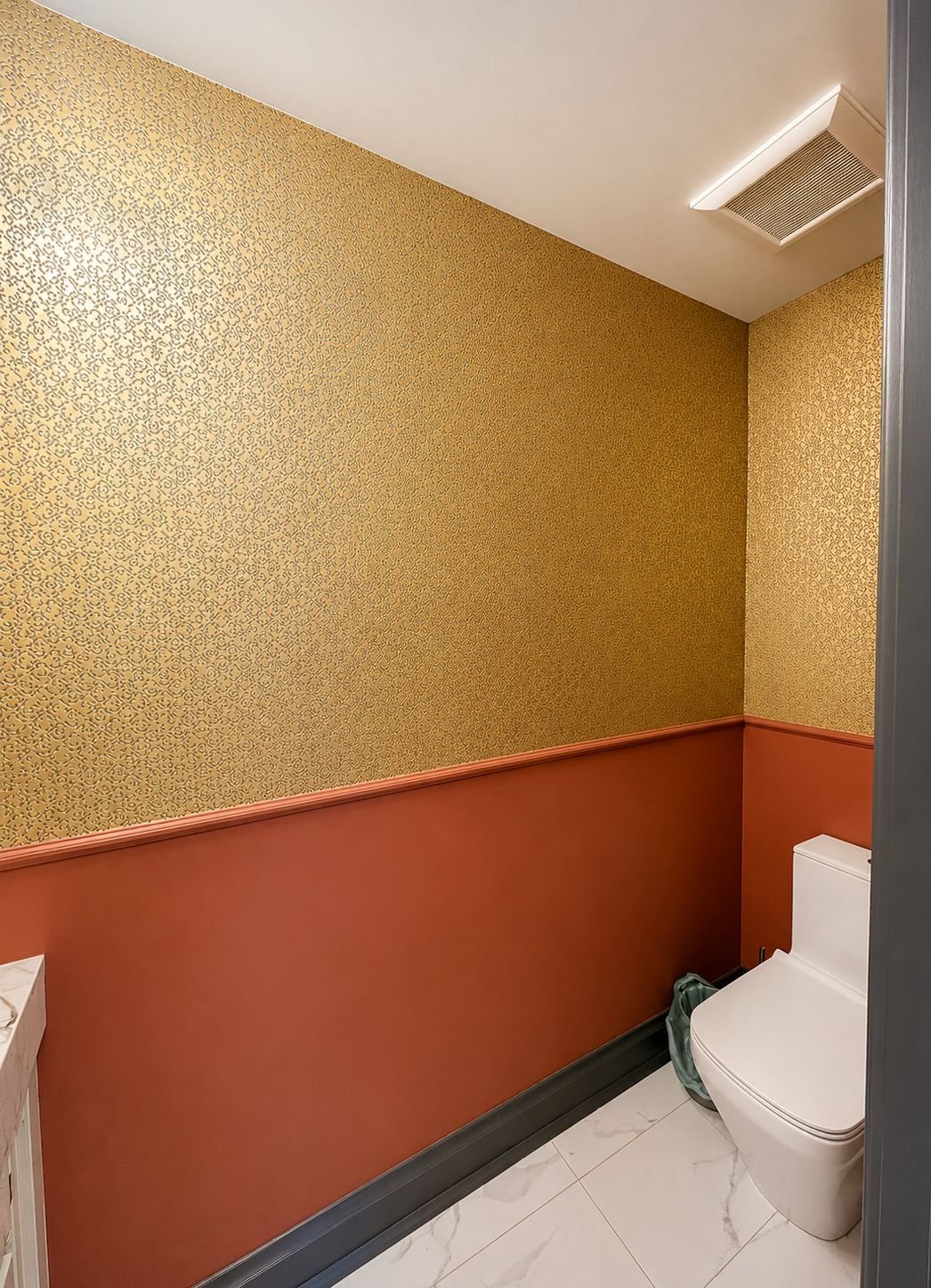 Powder room with textured gold wallpaper above a terracotta painted wainscot