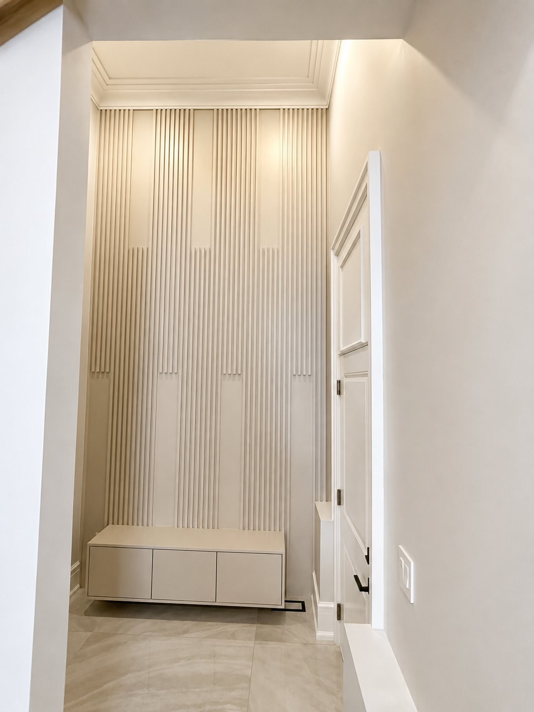 Spray-finished cream wood slat wall and built-in bench in an entry